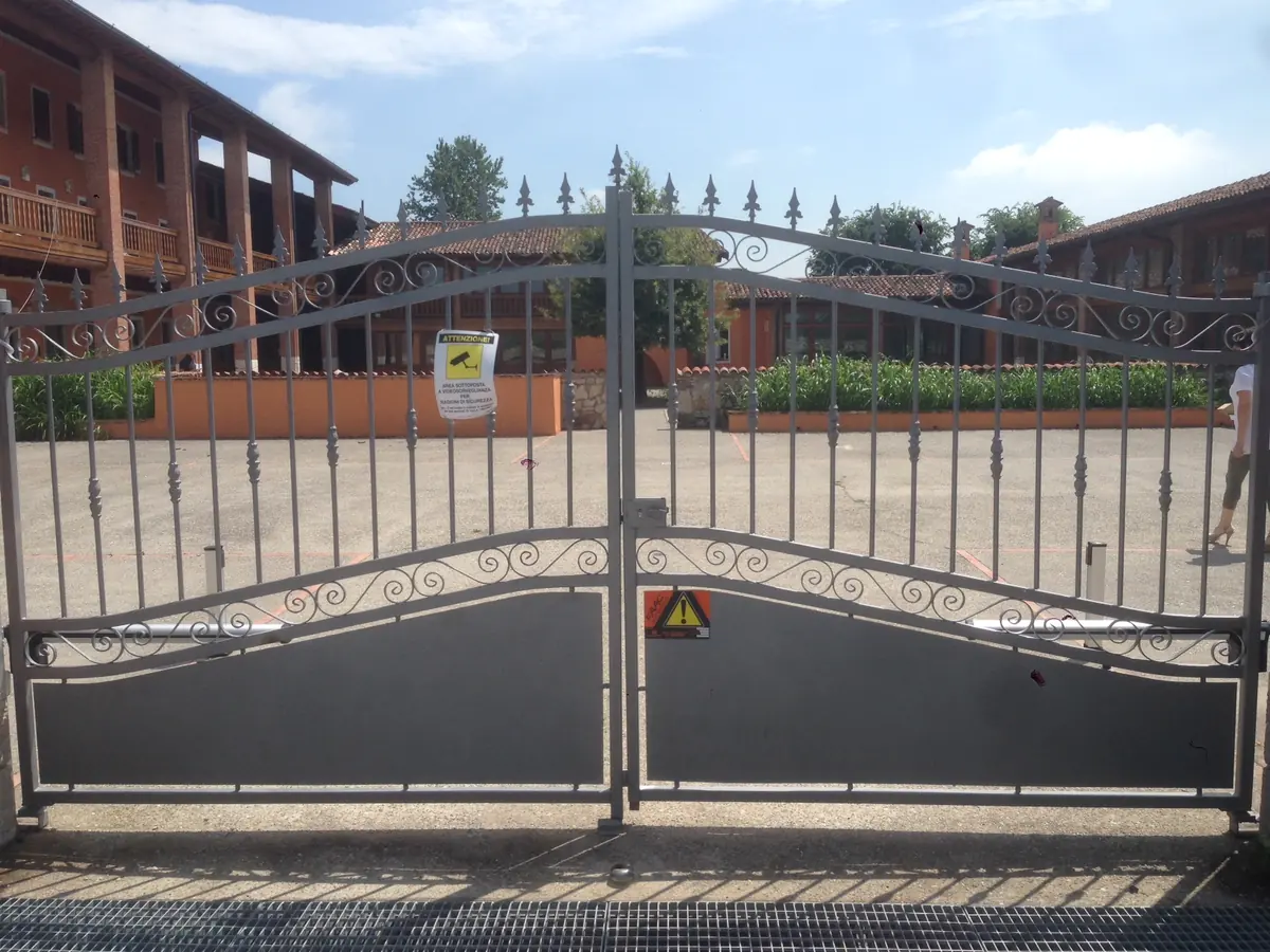 Cancello carraio a due ante in ferro battuto con automazione e segnaletica di sicurezza